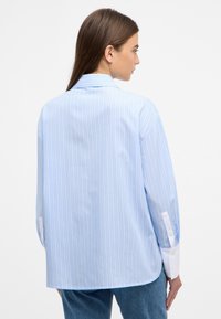 Blue striped shirt with long sleeves, white cuff accents, and a classic collar. Made of smooth fabric, featuring vertical stripes throughout.