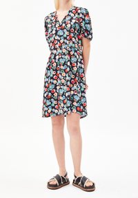 Robe à imprimé floral en tissu sombre, présentant un décolleté en V, des manches courtes bouffantes et une silhouette évasée simple ; portée avec des sandales noires plates.