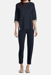 Mörkblå ribbad tröja med beige detaljer, halvlånga ärmar; ihop med mörkblå slim-fit byxor och ljusbeiga skor. Topp har rund halsringning.