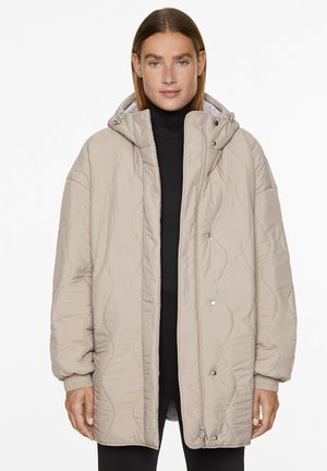 Beige quilted jacket with a hood, featuring a textured surface, snap and zip closure, and ribbed cuffs; designed for a loose fit.