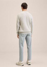 Maglione a maglia grigio chiaro con trama, vestibilità rilassata, abbinato a jeans azzurri. L'outfit include sneakers bianche e beige.