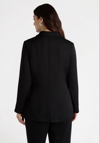 Sacou negru cu mâneci lungi, guler cu colțuri și un design drept pe spate. Material neted cu o croială ajustată.