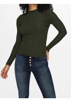 Top a maniche lunghe a coste di colore verde scuro con scollatura tonda e orlo ondulato. Abbinato a jeans di denim blu scuro con dettagli a bottoni.