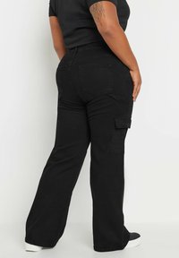 Svarta cargobyxor med hög midja. Dubbel bakfickor och sidoficka. Mjukt, tjockt tyg med rak benmeddelande.