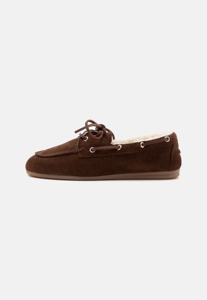 Bruine suède mocassinslof met leren veters en crèmekleurige fleece voering, zijaanzicht op een witte achtergrond.