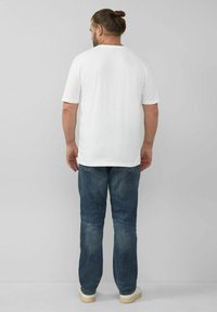Weißes T-Shirt mit kurzen Ärmeln, kombiniert mit blauen Jeans. Das Shirt hat eine lockere Passform; die Jeans sind leicht zulaufend mit einem umgeschlagenen Saum.