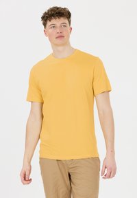 Gul bomullströja med rund halsringning och korta ärmar, i kombination med ljusbeige byxor. Slät textur, avslappnad passform.