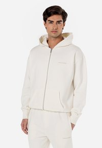 Hooded zip-up sweatshirt in cream. Soft fabric, spacious front pockets, and logo detail; relaxed fit with ribbed cuffs.