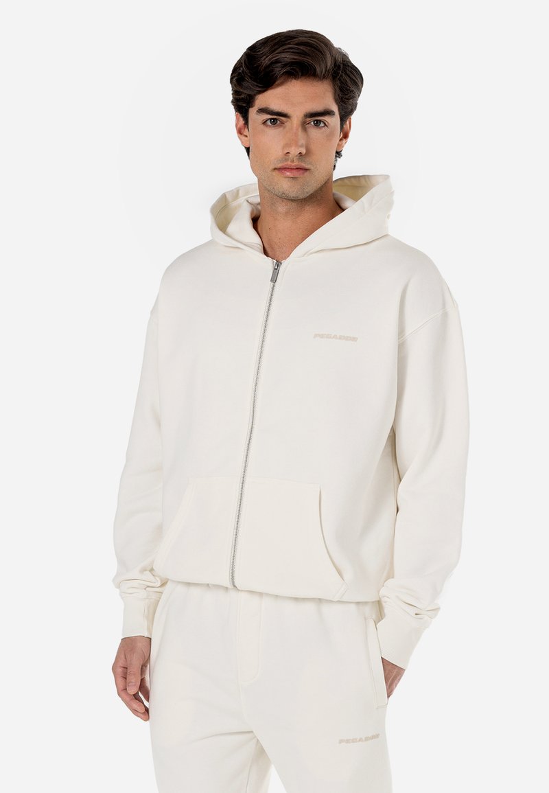Felpa con cappuccio e zip di colore crema. Tessuto morbido, ampie tasche frontali e dettaglio del logo; vestibilità rilassata con polsini a costine.