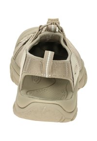 Beige outdoor shoe with a textured upper, elastic laces, and a pull tab at the heel. The sole is rugged for traction and stability.