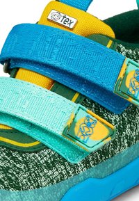 Baskets pour enfants en tissu tricoté vert, languette jaune, bandes auto-agrippantes bleu et turquoise, avec des motifs d'ours en peluche sur les fermetures à bandes.
