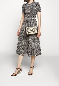 Svartvit mönstrad klänning med en figurnära byst och utställd kjol. Svart axelremsväska med en beige panel och cirkulär logotyp. Svarta remsandaler med klack.