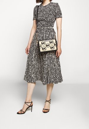 Vestito a fantasia in bianco e nero con corpetto aderente e gonna svasata. Borsa a tracolla nera con pannello color cuoio e logo circolare. Sandali neri con cinturini.