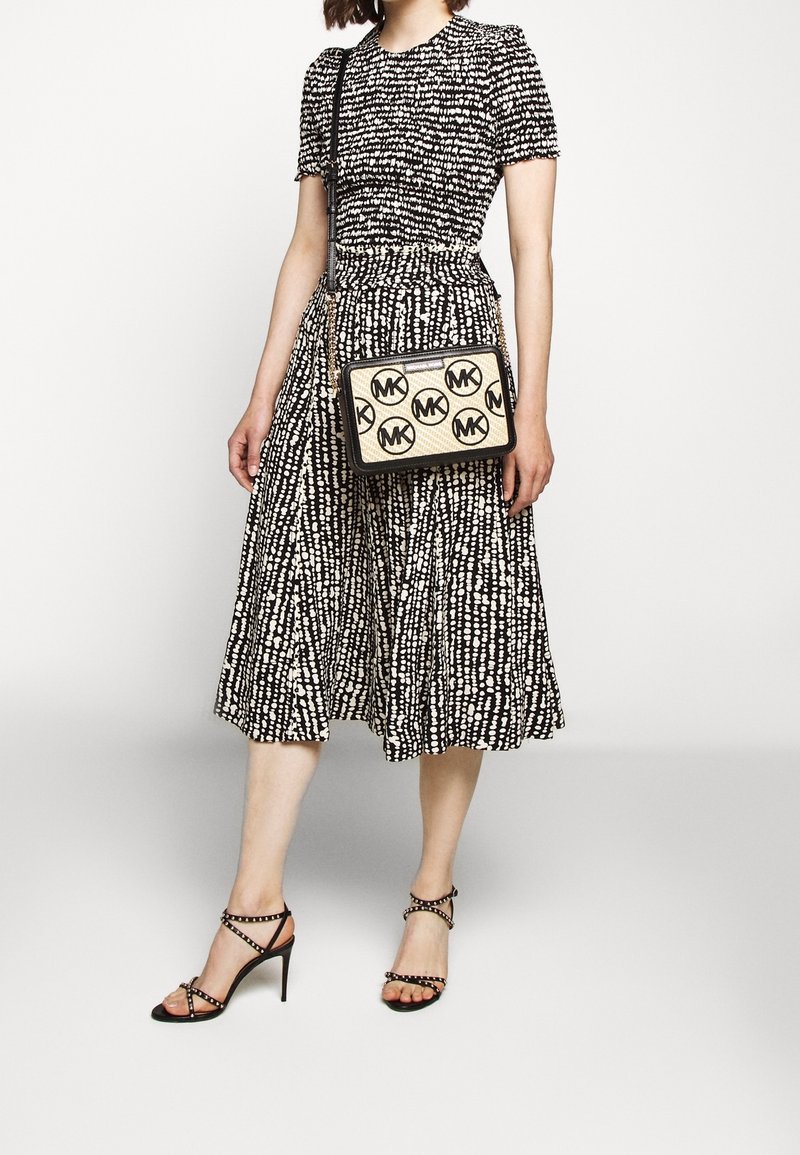Vestito a fantasia in bianco e nero con corpetto aderente e gonna svasata. Borsa a tracolla nera con pannello color cuoio e logo circolare. Sandali neri con cinturini.