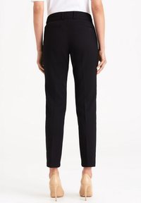 Pantalons noirs sur mesure, coupe ajustée, avec une ceinture à passants, deux poches arrière et des plis avant soigneusement repassés.