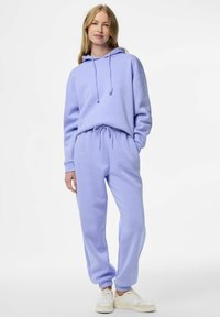 Světlofialová mikina s kapucí a odpovídající tepláky z měkkého materiálu. Mikina má šňůrky, kalhoty mají elastický pas a manžety.