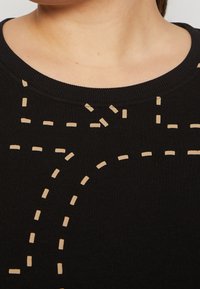 Svart tröja med rund halsringning, prydd med krämfärgade prickade linjer i olika mönster över tyget, vilket indikerar en unik design.