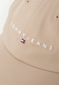 Beige stofkasket med broderet "TOMMYJEANS" tekst. Har et lille logo-patch i rød, hvid og blå på fronten.