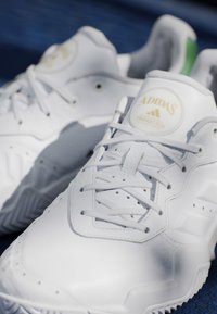 Sneakers bianche Adidas Tennis Club con lacci su una superficie blu, che mostrano cuciture dettagliate e il logo sulla linguetta.