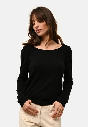Schwarzer, langärmeliger Pullover mit weitem Rundhalsausschnitt, strukturiertem Strickmuster und taillierter Silhouette, getragen mit cremefarbenen Hosen.