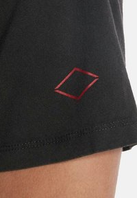 Tejido negro con un pequeño logotipo de diamante rojo en el dobladillo y una textura suave. costura visible a lo largo del borde.