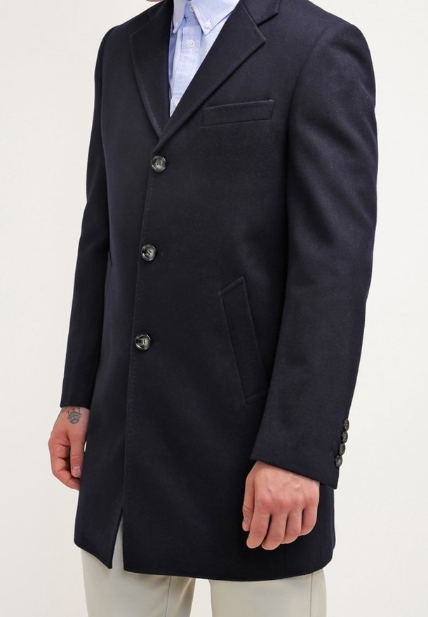 Marinblå ullrock med snedställda slag, fem knappar, två sidofickor och en bröstficka. Har textilstruktur och skräddarsydd passform.