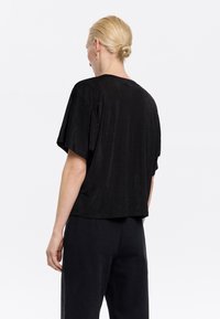 Top nero a maniche corte realizzato in un tessuto testurizzato con una vestibilità comoda. Design semplice senza motivi o decorazioni.