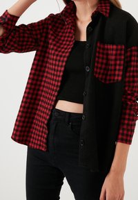 Camisa a cuadros rojos y negros con diseño de botones, de mangas largas y un bolsillo en la parte izquierda. Textura de mezcla de algodón.