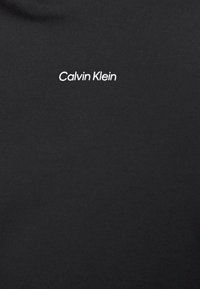 Camiseta de algodón negra con un logo blanco de "Calvin Klein" en la zona izquierda del pecho. Textura suave con un diseño clásico de cuello redondo.