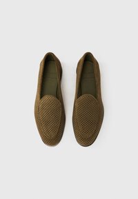 Καφέ δερμάτινα μοκασίνια από σουέτ με διάτρητο σχέδιο, στρογγυλεμένη μύτη και λεπτομέρειες κατά μήκος των άκρων. Μαλακή εσωτερική επένδυση και επίπεδη σόλα.