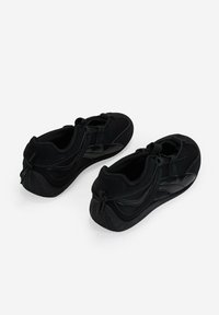 Zapatos negros con parte superior de textil suave y suela de goma. Presentan cordones elásticos y un cuello acolchado. Punta redonda y suela texturizada.