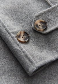 Deux gros boutons marbrés marron et noir sur le poignet d'un manteau en laine gris.