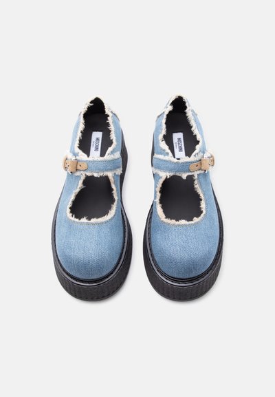 Chaussures Mary Jane en jean bleu clair avec bords effilochés, brides à boucle beige, semelles épaisses noires, et étiquette de la marque Moschino à l'intérieur.
