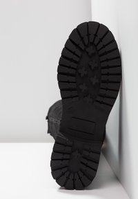 Semelle de botte en caoutchouc noir présentant un motif de bande de roulement robuste, avec des rainures profondes et des formes croisées surélevées pour l'adhérence.