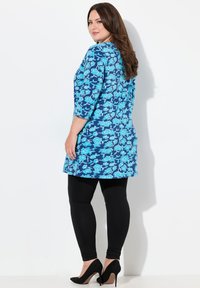 Blå blommig tunika med trekvarts ärmar, kombinerad med svarta leggings och svarta klackar. Har en livlig tryck på ett mjukt tyg.