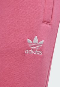 Ružové teplákové nohavice Adidas s textúrovanou tkaninou. Obsahujú biele vyšívané logo trefoil a dizajn troch pruhov.