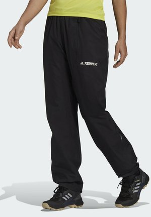 Black waterproof hiking pants with elastic waistband, zip pockets, and "TERREX" logo in white. Paired with black trail shoes featuring gray stripes.