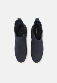 Marineblå slippers i semsket skinn med elastiske sidepaneler, hvite gummisåler og en jevn tekstur. Merking synlig inni.