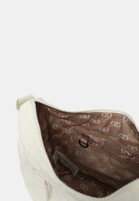 Borsa bianca con materiale esterno testurizzato, dotata di una fodera marrone a motivo. L'interno include una tasca con zip e un compartimento in rete.