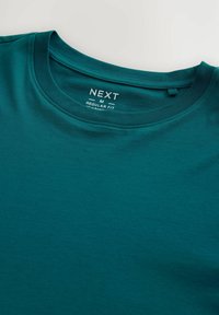 Camiseta de algodón en color aguamarina con cuello redondo, corte regular y una etiqueta que muestra el nombre de la marca y la talla. Textura suave con costuras lisas.