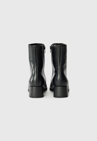 Botines de cuero negro con una textura suave, cierre de cremallera en la parte trasera y un tacón rectangular grueso.