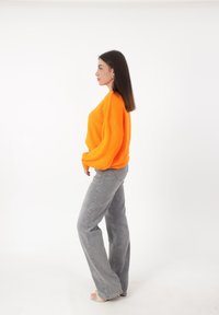 Orangenes, übergroßes Strickpullover mit langen Ärmeln, kombiniert mit hellgrauen, ausgestellten Jeans. Glatte Textur und lässige Passform. Schlichte Sandalen.