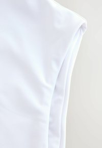 Witte mouwloze kledingstuk gemaakt van een gladde, lichtgewicht stof. Heeft een ronde halslijn en zacht gebogen armsgaten.