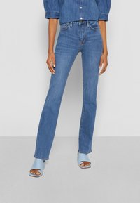 Jeans de denim azul con un ajuste ajustado, una cintura de altura media y un ligero acampanado en el dobladillo. La tela tiene una textura suave y detalles de desvanecimiento sutiles.