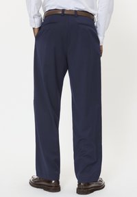 Granatowe spodnie o szerokich nogawkach z gładkiego materiału, z dwiema tylnymi kieszeniami i brązowym skórzanym paskiem, noszone z ciemnymi butami.