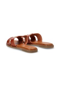 Sandalias deslizantes de cuero marrón con diseño troquelado y suela beige. Presenta una textura suave y costuras blancas a lo largo del borde.