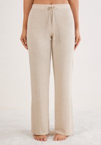 Pantalons de lounge beige en tissu doux et respirant. Caractéristiques d'une coupe décontractée, d'une taille à cordon de serrage et de jambes larges pour le confort. Texture plate, sans motifs.