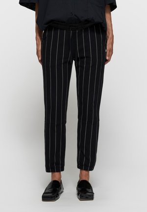 Czarne spodnie w paski wykonane z elastycznego materiału, z regulowanym paskiem w talii, zwężanymi nogawkami i gładką fakturą.
