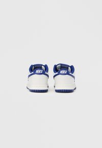 Białe sneakersy Nike z niebieskimi akcentami, z teksturowaną skórzaną cholewką, wyściełanym kołnierzem i niebieską gumową podeszwą.