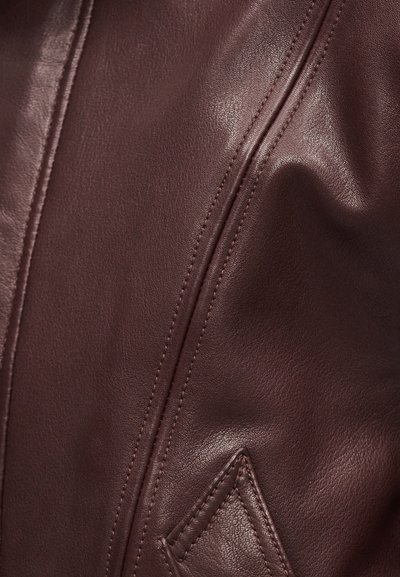 Κοντινό πλάνο από ομαλό καφέ δέρμα με λεπτομερείς ραφές και ένα μικρό έμπλαστρο σε σχήμα διαμαντιού.